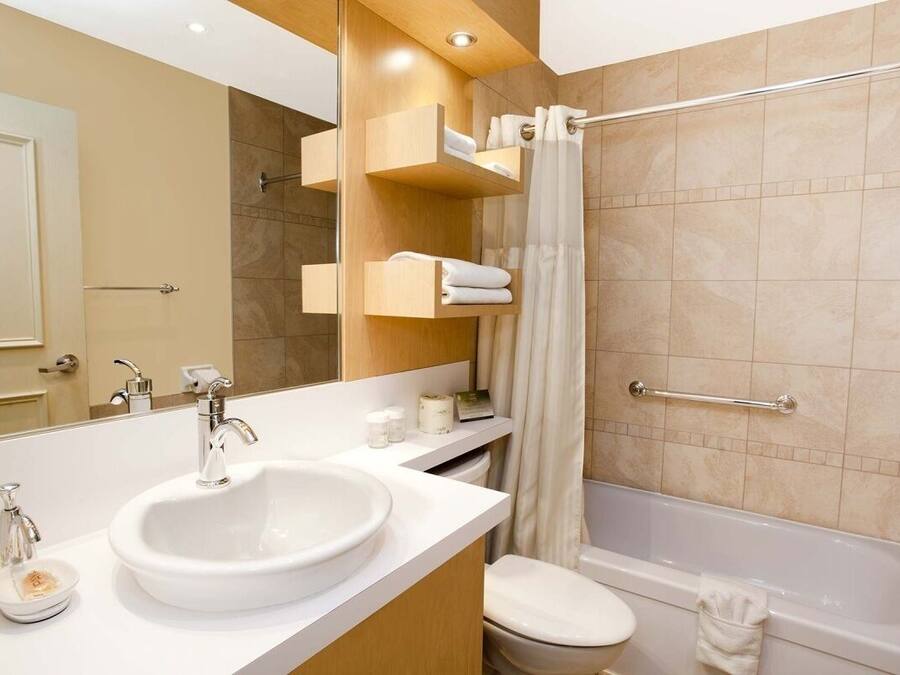 A modern bathroom with a large sink, toilet, and bathtub. There are wooden shelves with towels and toiletries.