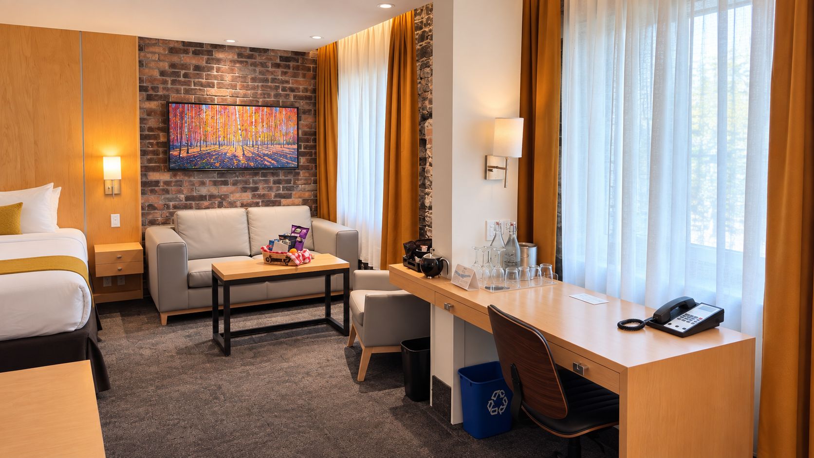 Habitación de hotel con cama, sofá, escritorio y mesa de centro. Se observa un cuadro en la pared, una lámpara y un teléfono sobre el escritorio.
