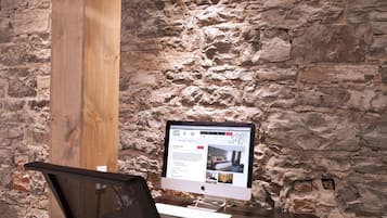 A modern office space with a stone wall, a wooden pillar, a desk with a computer, and a mesh office chair.