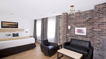 Een moderne hotelkamer met een bed, twee zwarte leren banken, een houten salontafel en een accentmuur van baksteen.