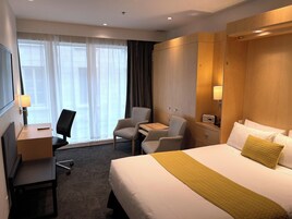 Una habitación de hotel con cama, escritorio, silla, televisor y ventana con cortinas.