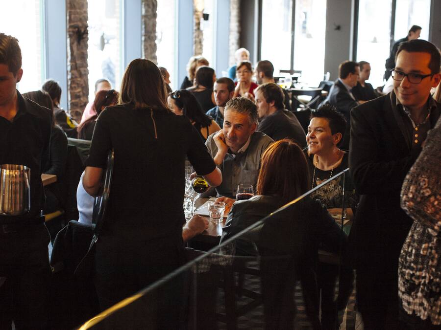 A crowded indoor space with people standing and sitting at tables, suggesting a social event or gathering.