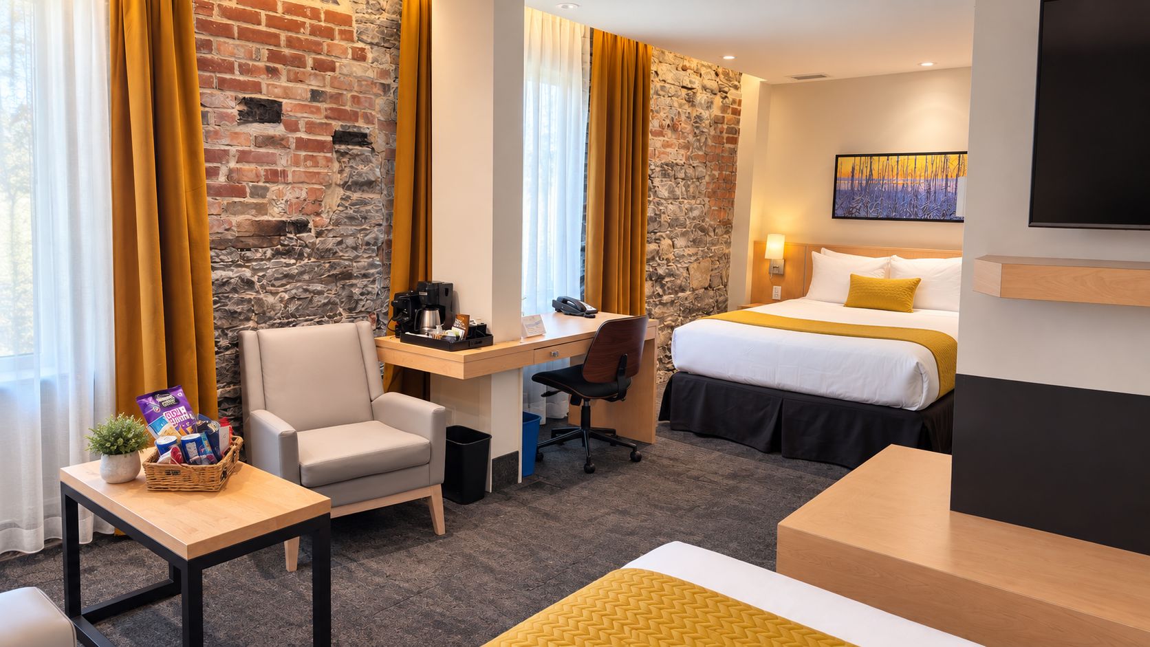 A hotel room with a desk, chair, bed, and a stone wall.