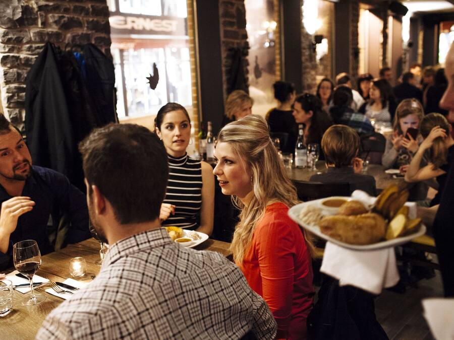 Un restaurante concurrido, con comensales sentados en mesas, algunos con platos de comida y bebidas.