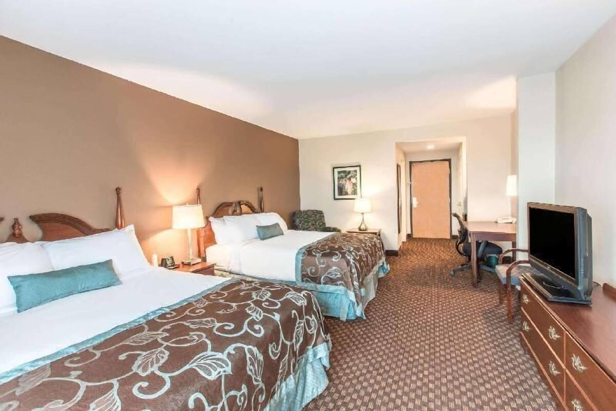A hotel room with two beds, a desk, a television, and a door leading to another room.