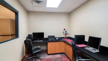A corner office with two desks, each with a computer and a chair. There is a window on the left and a ceiling light.