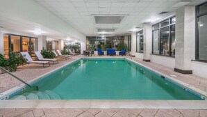 An indoor swimming pool with lounge chairs and tables, surrounded by large windows and indoor plants. - Wingate by Wyndham Lexington (Lexington)