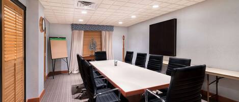 A conference room with a long table, black chairs, a whiteboard, and a clock on the wall.