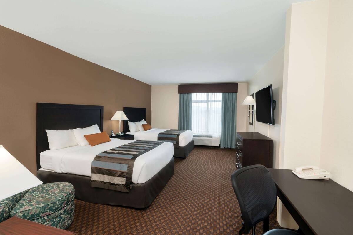A hotel room with two beds, a desk, a chair, a TV, and a telephone.