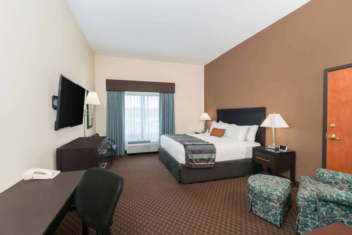 A hotel room with a bed, bedside tables, a desk, a chair, and a TV.