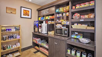 A kitchenette area with a coffee machine, microwave, and various food items on shelves.