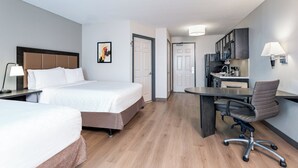 A hotel room with two beds, a desk, and a kitchenette.