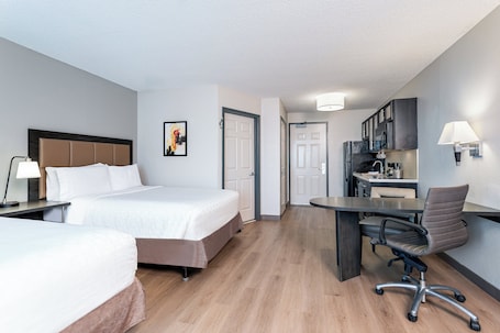 A hotel room with two beds, a desk, and a kitchenette.