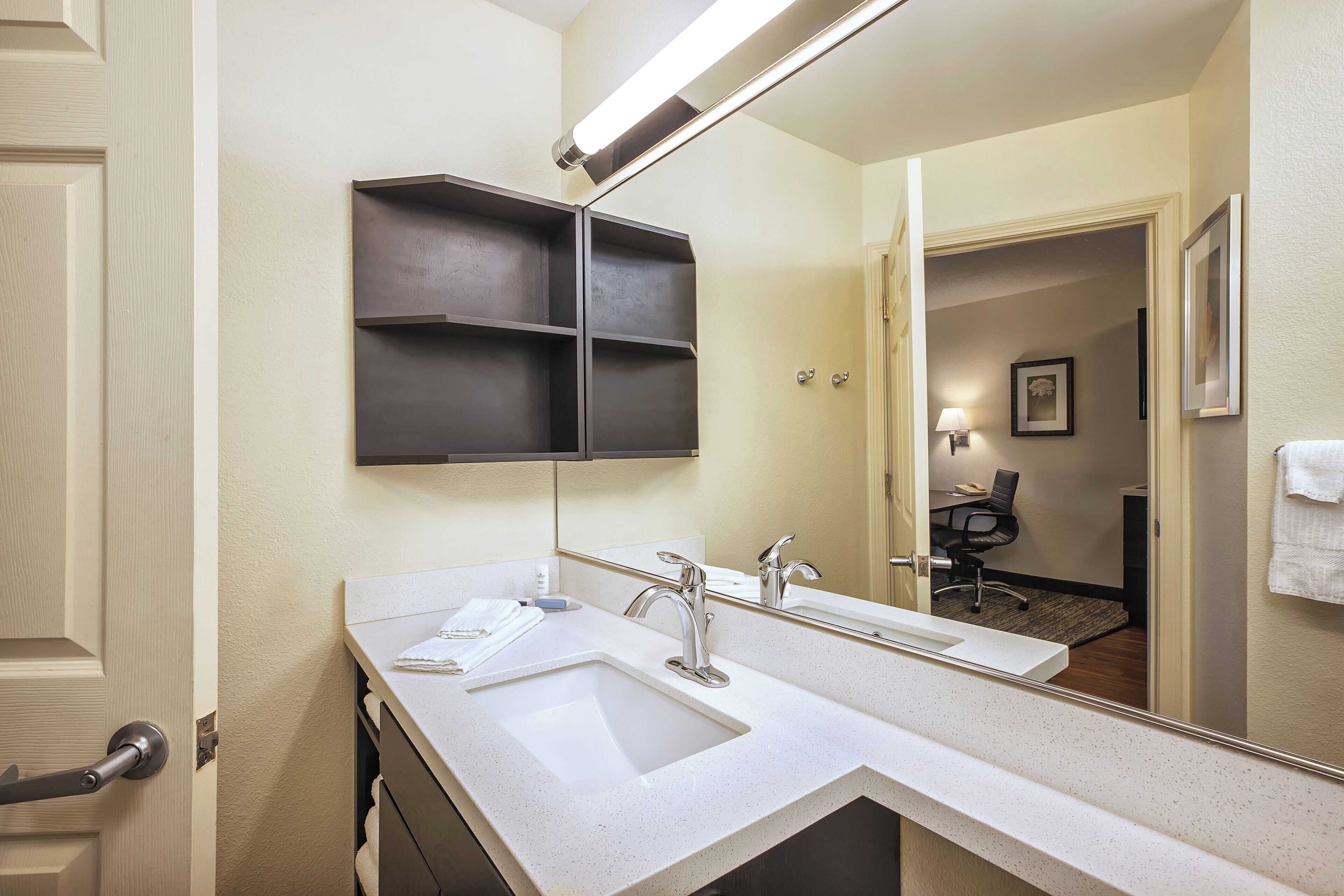 A hotel bathroom with a double sink, a large mirror, and a towel rack.