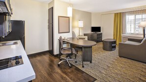 A hotel room with a kitchenette, a dining table, a sofa, a TV, and a lamp.
