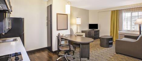 A hotel room with a kitchenette, a dining table, a sofa, a TV, and a lamp.