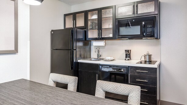 A compact kitchen with a refrigerator, microwave, and dishwasher. There is a dining table with two chairs.