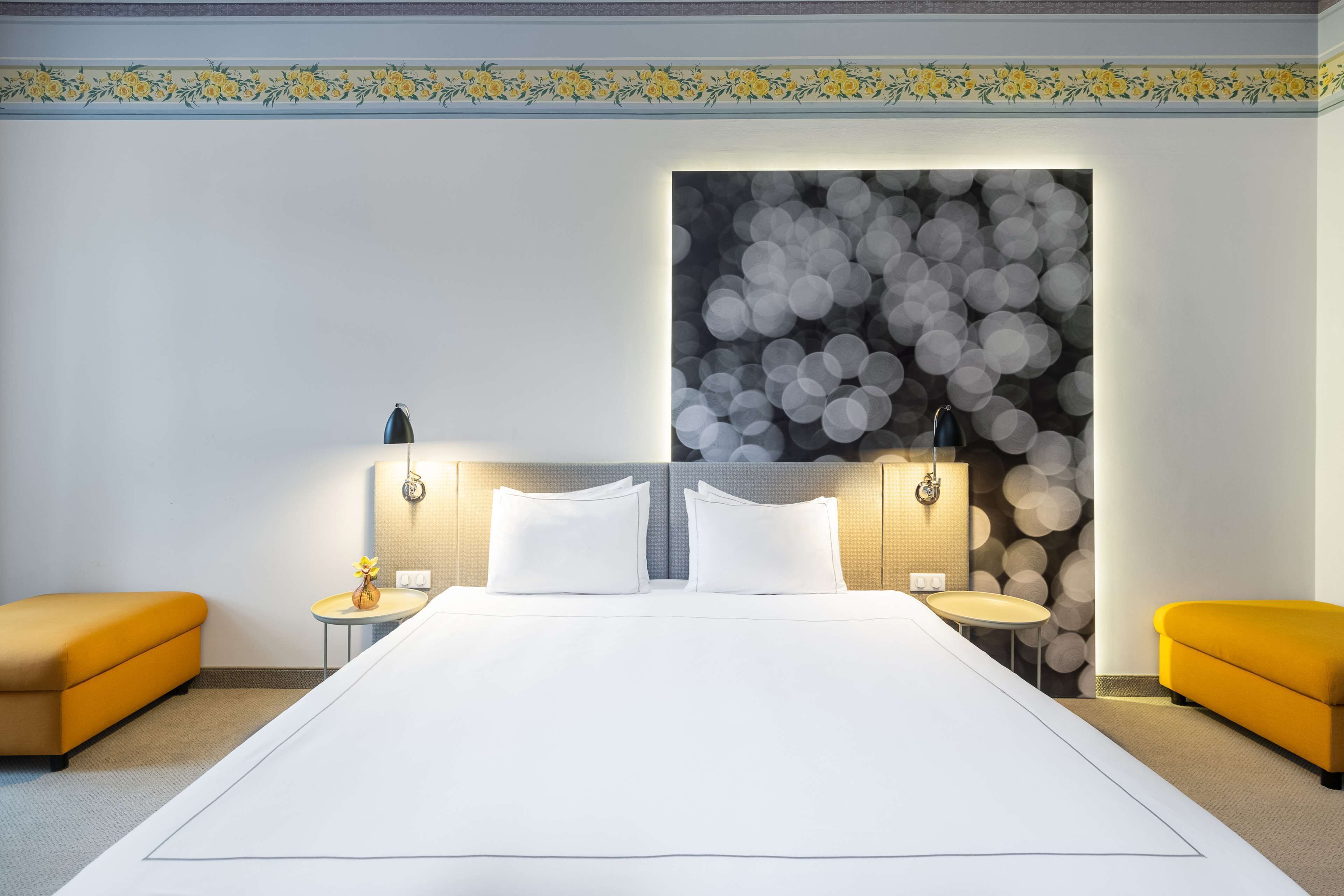 A large bed with white linens, two bedside tables with lamps, and a wall with a circular bokeh pattern.