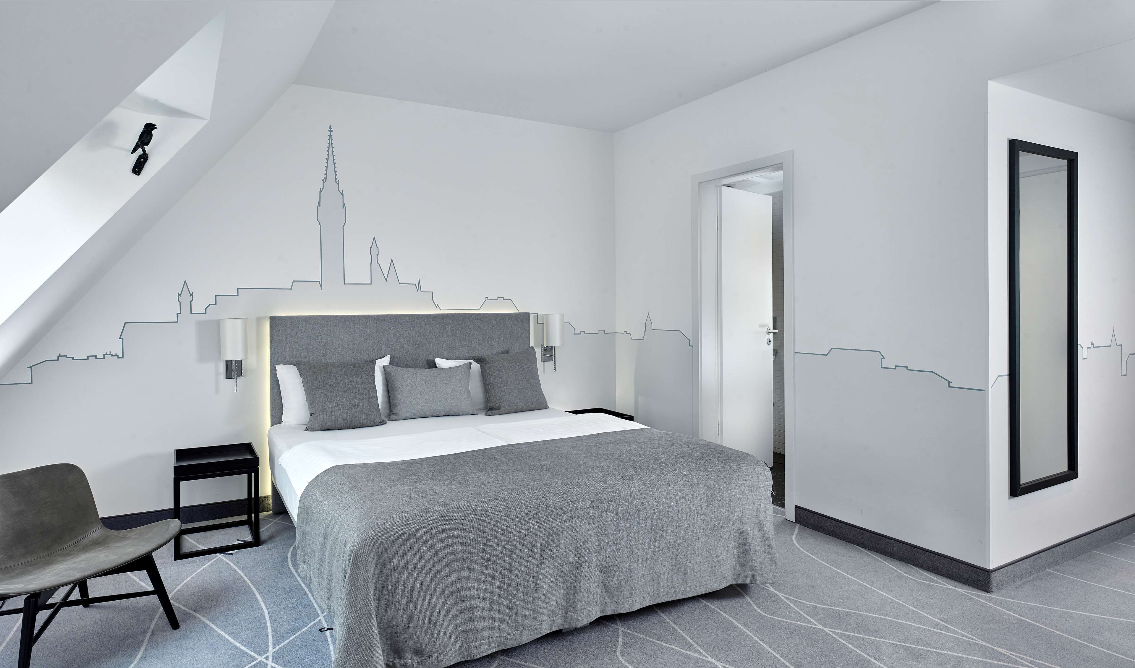 A modern bedroom with a bed, a chair, and a city skyline wall art.