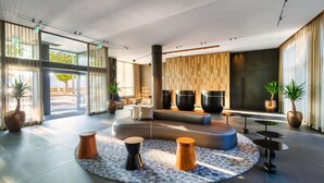 Eine moderne Lobby mit einer gebogenen Sitzecke, großen Kübelpflanzen und einem gemusterten Teppich.