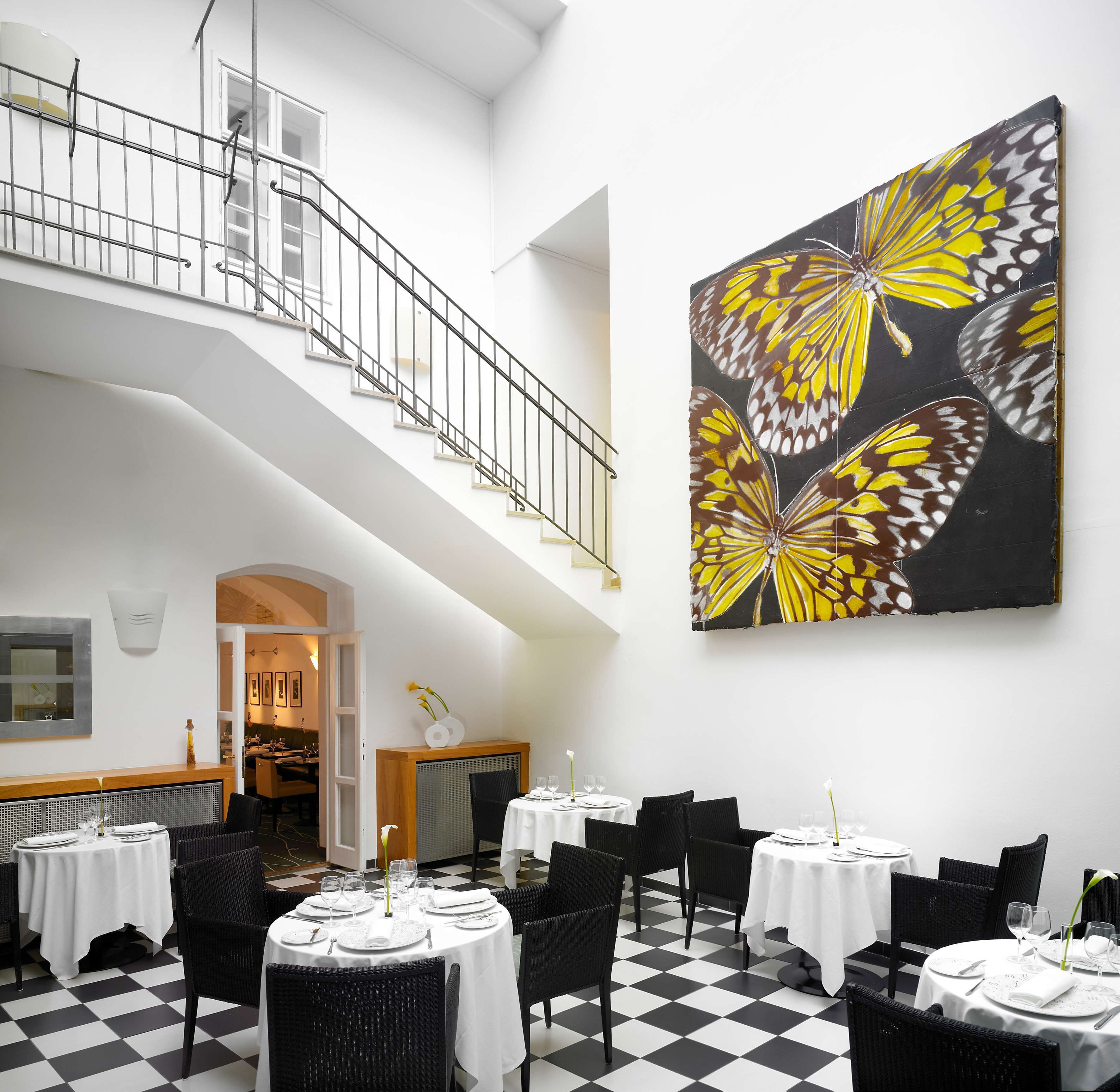 Un comedor con suelo a cuadros, varias mesas redondas dispuestas para comer y una escalera que lleva a un nivel superior.