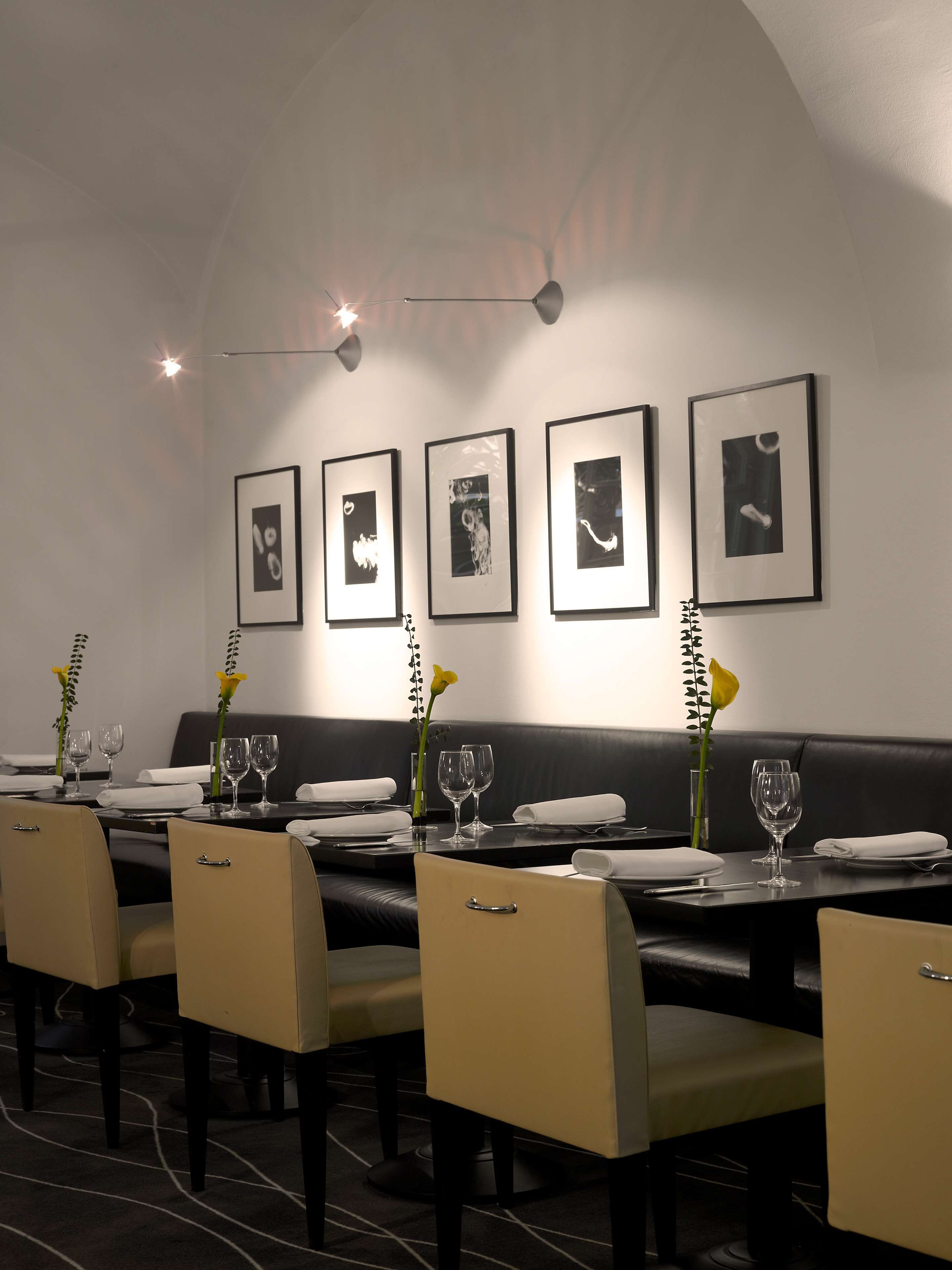 Een restaurant met een modern interieur, met zwart-wit kunstwerken in lijsten aan de muur, netjes gerangschikte tafels met stoelen en een minimalistische inrichting.
