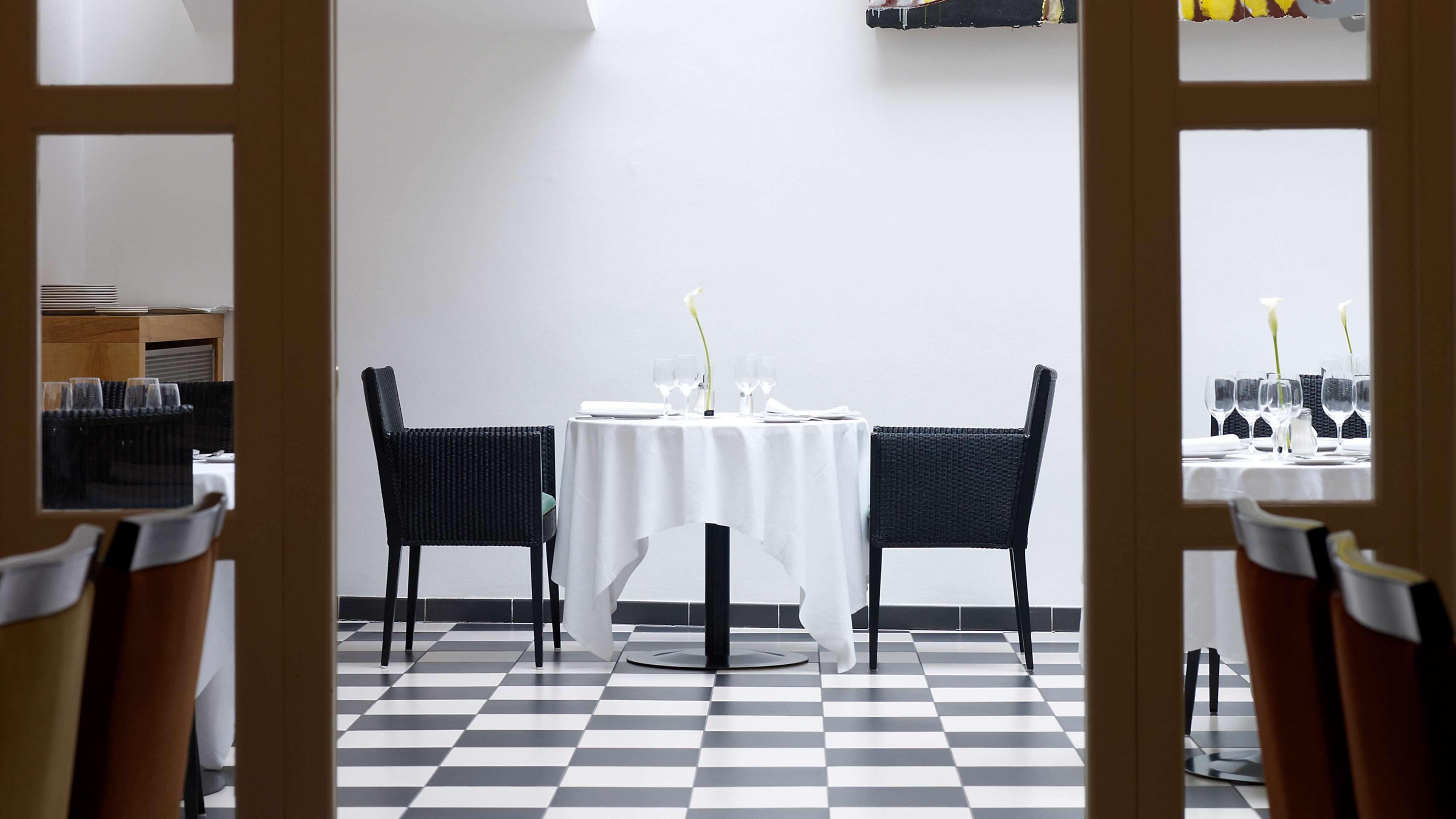 A dining area with a checkered floor, two black chairs, a round table, and a white tablecloth.