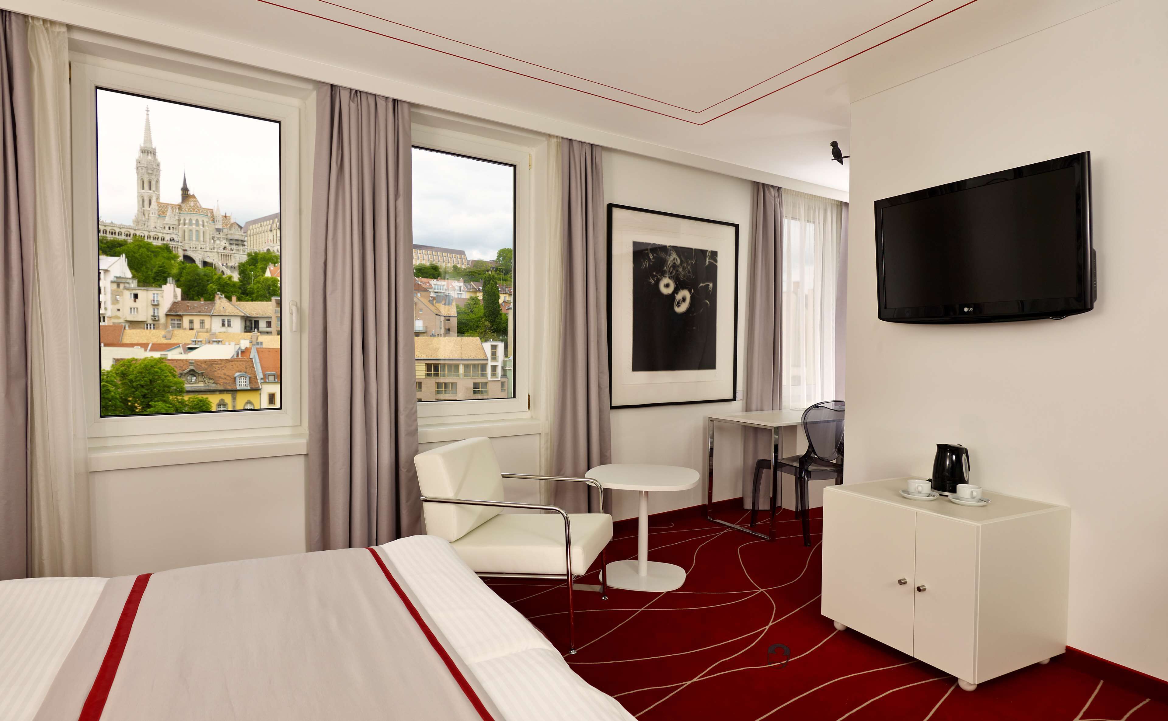 Habitación de hotel con cama, escritorio, silla, televisión y vista panorámica de la ciudad.