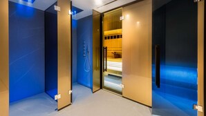 Ein modernes Hotelzimmer mit Glastrennwand, Duschbereich und einem Bett mit Holz-Kopfteil.