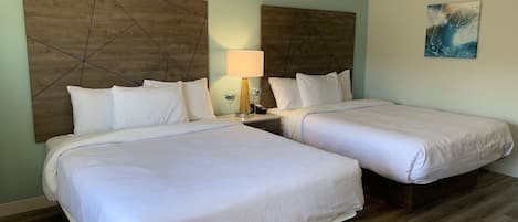Habitación de hotel con dos camas, cabecera de madera, lámpara de noche y un cuadro en la pared.