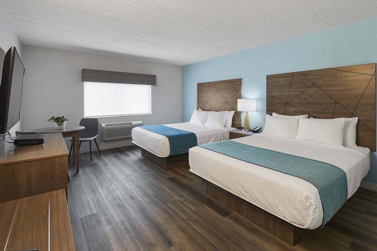 A hotel room with two beds, a desk, a chair, a TV, and a window.
