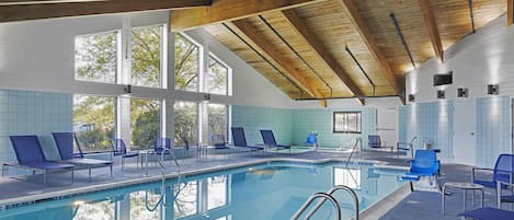 A swimming pool with blue lounge chairs and a wooden ceiling.