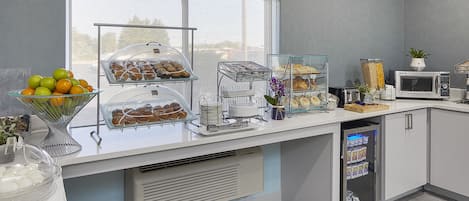 A modern kitchen with a breakfast bar featuring a variety of pastries, fruits, and a coffee machine.