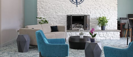 A modern living room with a stone fireplace, a large compass wall decoration, and two blue armchairs.