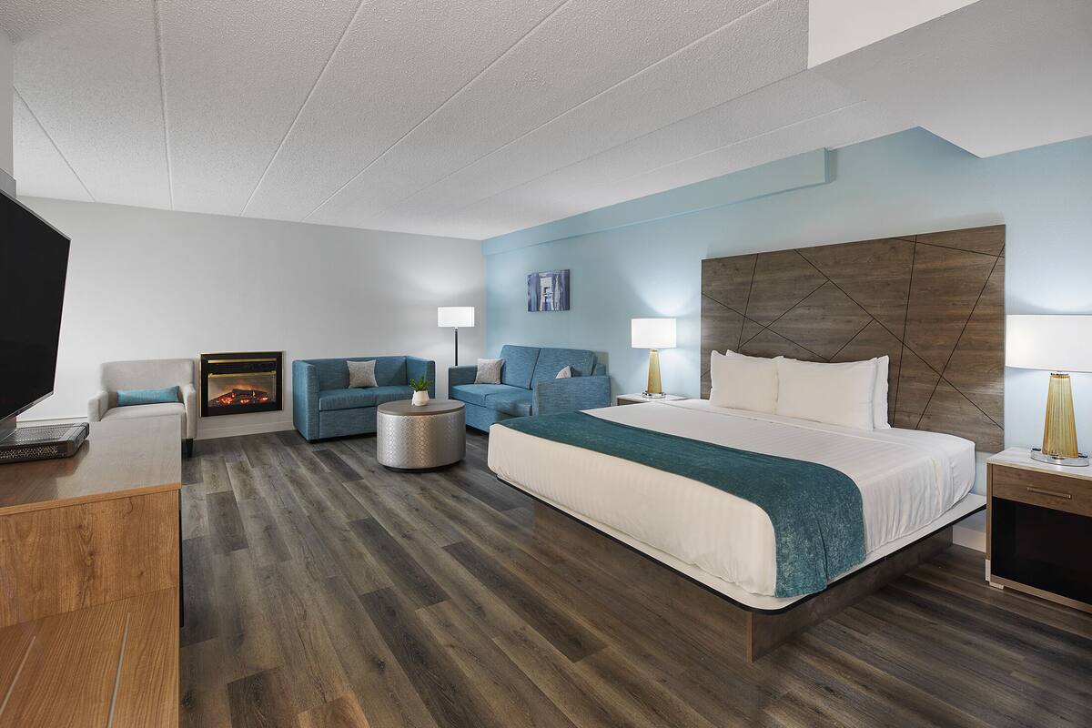 A modern hotel room with a large bed, two sofas, a TV, and a fireplace.