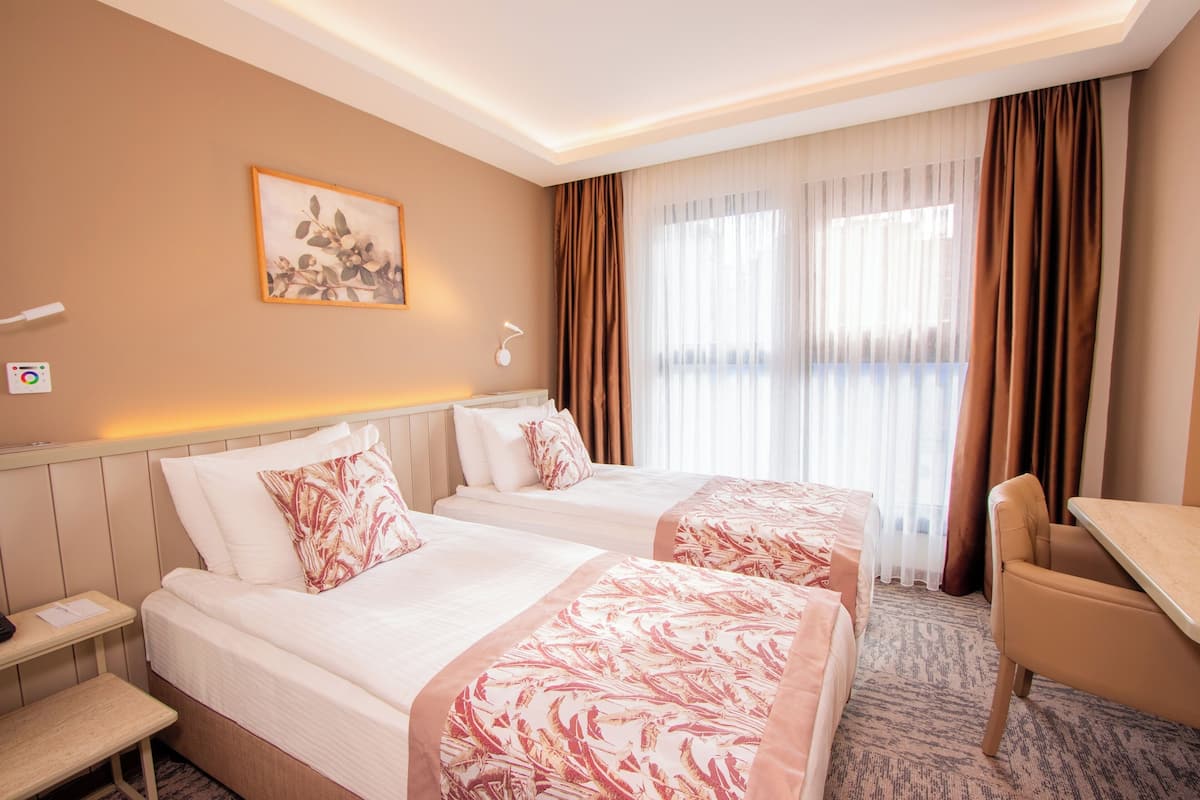 A hotel room with two beds, a desk, a chair, a nightstand, and a painting on the wall.