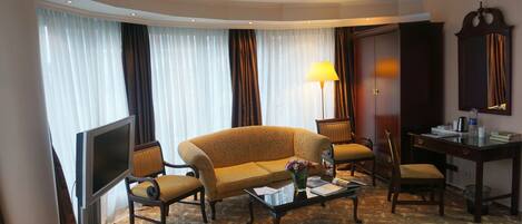 Una habitación de hotel con sofá, sillones, escritorio, televisor y cama.