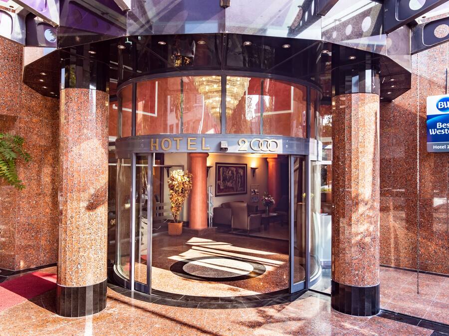A hotel entrance with a glass door, a sign indicating it's the Best Western Hotel 2000, and a lobby area visible through the glass.