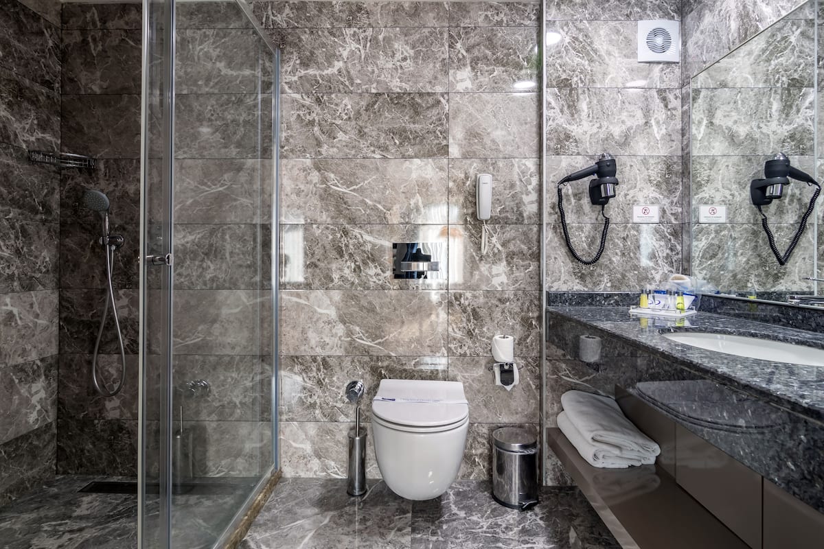 A modern bathroom with a glass-enclosed shower, a white toilet, a sink with a marble countertop, and a mirror.
