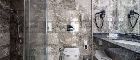 Un baño moderno con cabina de ducha de vidrio, inodoro blanco, lavabo con encimera de mármol y espejo.