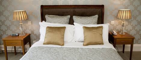 Una cama bien hecha con una colcha estampada, dos mesitas de noche con lámparas y un cuadro en la pared.