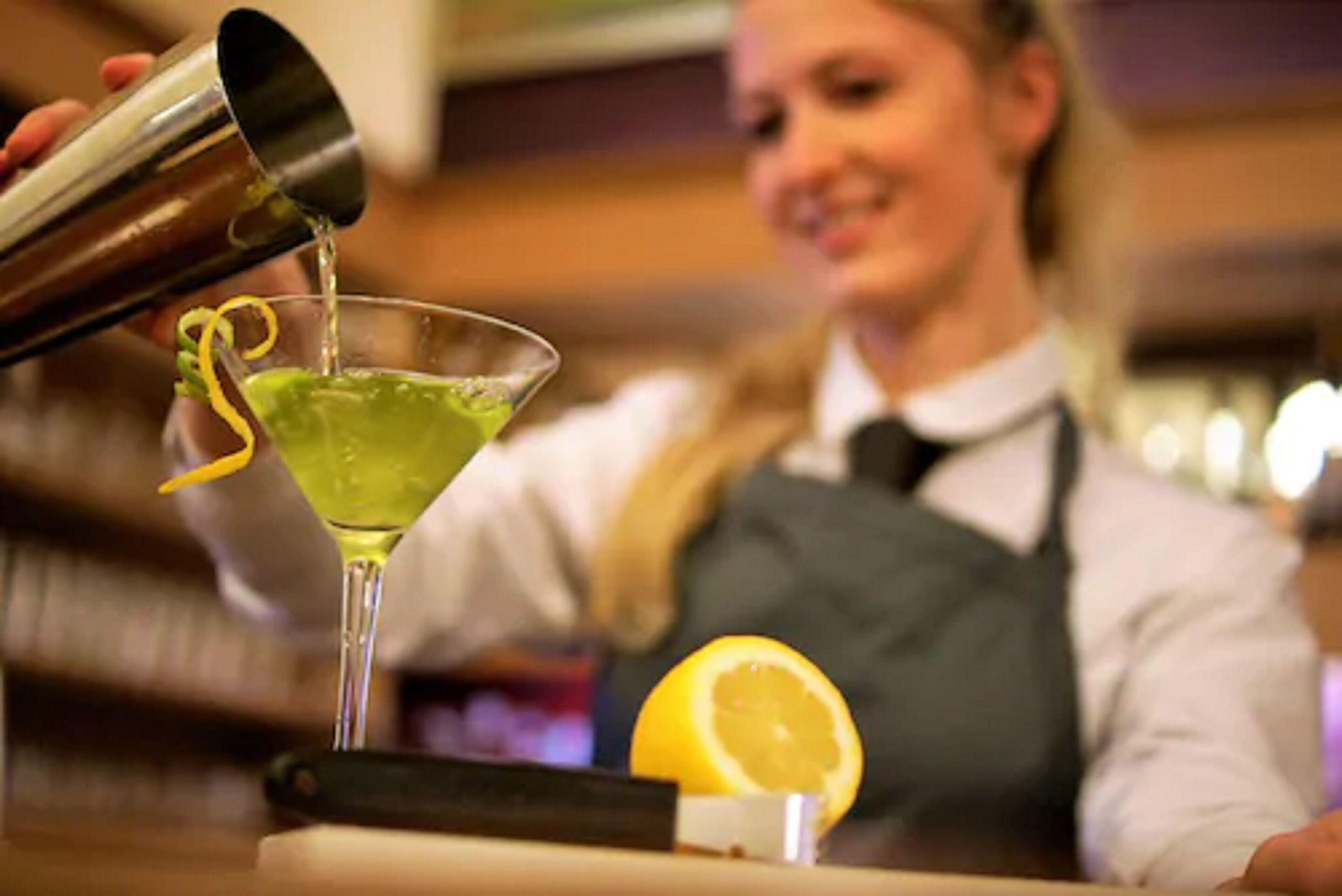 A bartender pouring a drink into a martini glass.