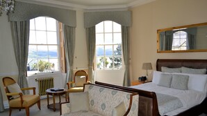 Habitación de hotel con una cama grande, dos sillones, una mesita y vistas al exterior a través de dos ventanas.