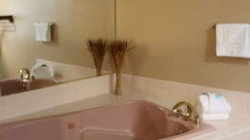 Un baño con una bañera rosa grande, azulejos blancos, un espejo y dos plantas decorativas.