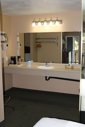 A hotel bathroom with a large mirror, a sink, a hairdryer, and a towel rack.