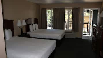 Habitación de hotel con dos camas, una mesita de noche con lámparas, un aparador y vistas al exterior a través de una ventana con cortinas.