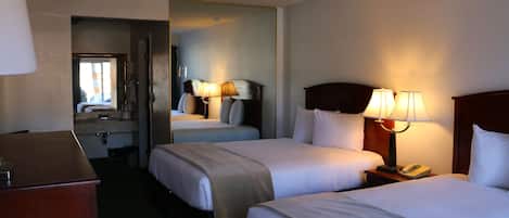 Habitación de hotel con dos camas, un escritorio y un baño visible a través de una puerta abierta.