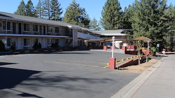 A motel with a parking lot, a covered outdoor seating area, and a building with multiple windows and balconies.