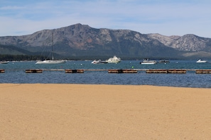A beach with a row of boats docked in the water, a mountain range in the background, and a clear sky.