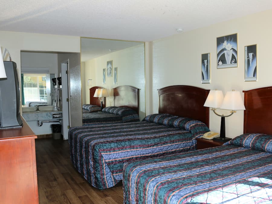 A hotel room with two beds, a desk, a mirror, and a nightstand with lamps.